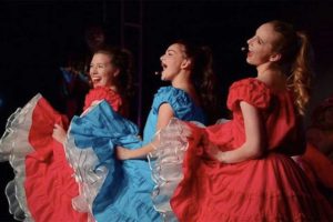 three young women dancing in bright red and bright blue dresses. they are singing