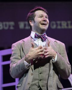 man in costume singing onstage with superscript text behind him