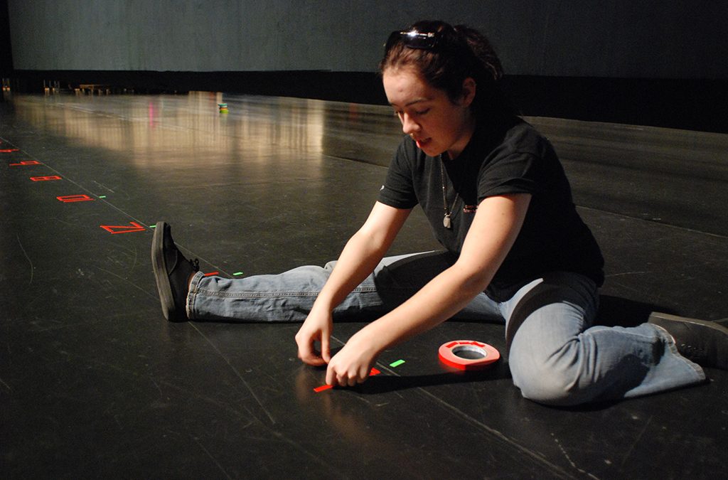 A Thespian tapes spike marks on the International Thespian Festival main stage.