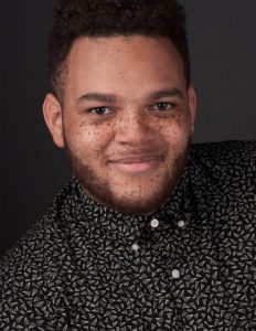 A young black man wearing a button-down shirt smile for the camera.