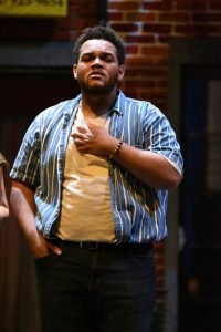 A young black man stands onstage and delivers a monologue.