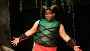 A young Black actor stands on stage in a horned costume.